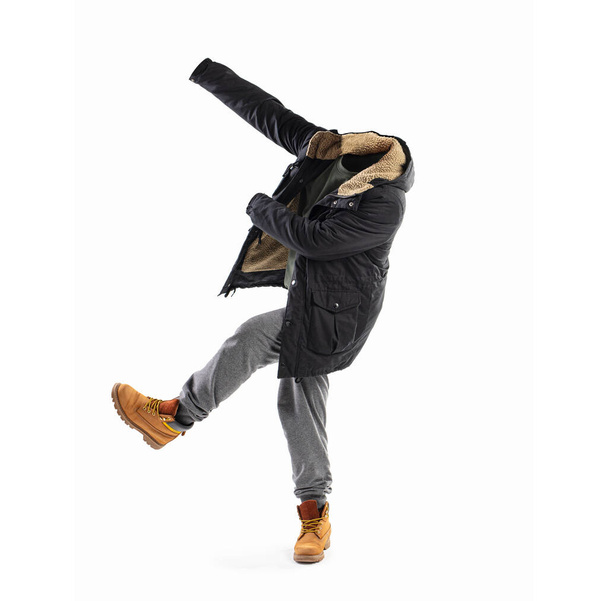 Hombre invisible saltando con los brazos extendidos, llevando una chaqueta, sombrero, pantalones de chándal y botas anaranjadas aisladas en blanco. Concepto de cartel - Foto, Imagen
