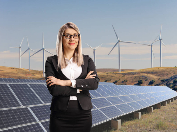 Businesswoman standing on a sustainable energy solar panel field with wind turbines - Фото, изображение