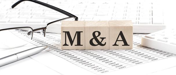 M and A written on a wooden cube with keyboard , calculator, chart,glasses.Business concept - Photo, Image