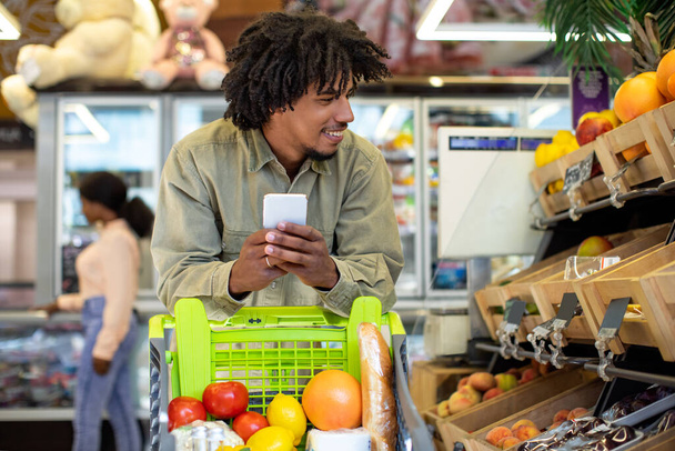 Black Guy faisant du shopping à l'aide d'un téléphone portable achetant de la nourriture dans un supermarché - Photo, image