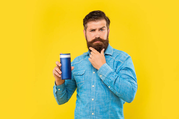 brutal man hold shampoo bottle on yellow background, haircare. touch beard - Photo, image