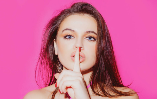 Beauty woman. Portrait of pretty mysterious girl showing silence shh sign holding forefinger on lips on pink background. - Photo, image