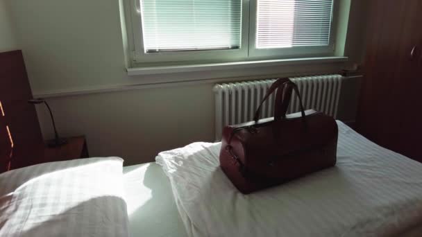 Egy barna utazótáskát helyeztek el egy hotelszobában, amit a reggeli nap világított meg. - Felvétel, videó