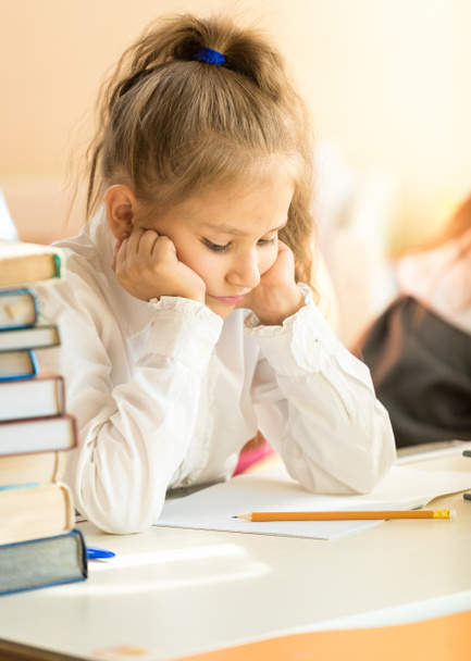 Portrait of upset schoolgirl looking at textbook with homework - Photo, Image