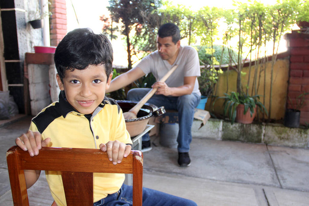 Papa et fils latins cuisinent ensemble le traditionnel mole rojo mexicain dans un pot en argile avec une cuillère en bois comme une activité familiale de fierté, de culture et de tradition - Photo, image