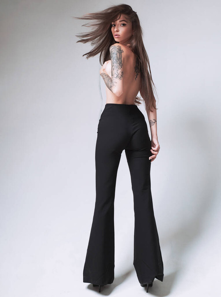 Tall slim lady. Topless model wear high waist pants. Tattooed sensual model long hair. Fashion concept. Windy hairstyle. Girl attractive fashion model. Vogue and fashion. Gorgeous pretty woman - Fotografie, Obrázek