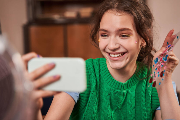 Female teenager posing to the selfie camera of smartphone with rhinestones - Photo, image