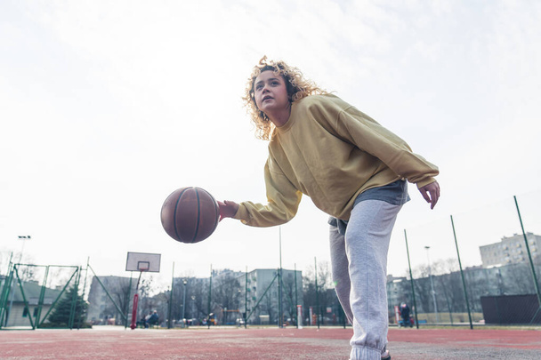 Young blond Caucasian woman plays basketball in baggy clothes, looking up copy space medium full shot  - Foto, immagini