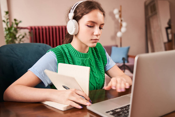 Serious female teenager enjoying of the distance learning while sitting in front of the laptop - 写真・画像