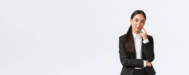 Kreatív okos ázsiai női menedzser, ügynök öltönyös mosolygós ravasz és belenéz a kamerába, van terv, gondolkodás, van kiváló ötlet, állva elégedett fehér háttér - Fotó, kép