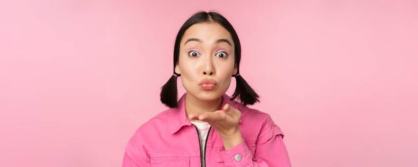 Detail portrét krásné hloupé asijské dívky, posílání vzduchu polibek, mwah na kameru, foukání, stojící nad růžovým pozadím - Fotografie, Obrázek