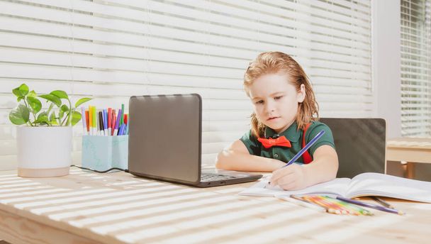 Cute schoolboy child does her homework with a tablet or laptop at home. Pupil writes the task in a notebook. Education and learning, kids home schooling. - Φωτογραφία, εικόνα
