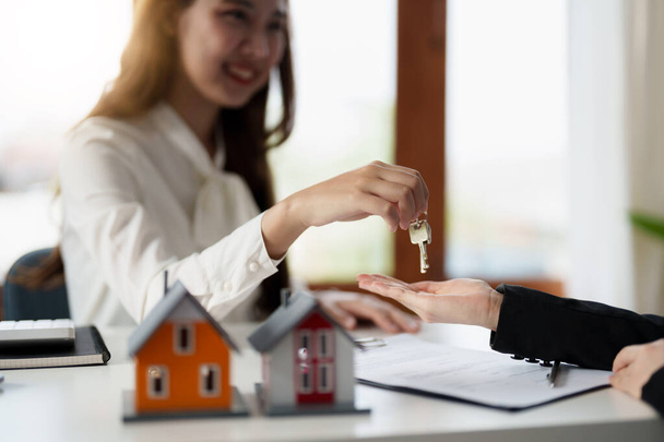 Real estate agent holding house key to his client after signing contract agreement in office,concept for real estate, moving home or renting property - 写真・画像