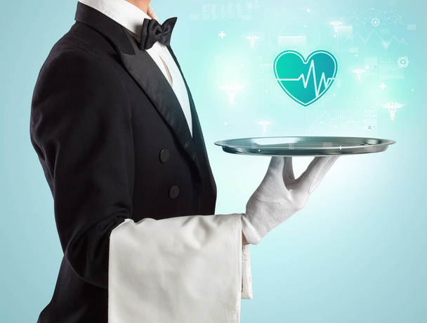 Handsome young waiter in tuxedo holding healthcare icons on tray - Foto, Bild