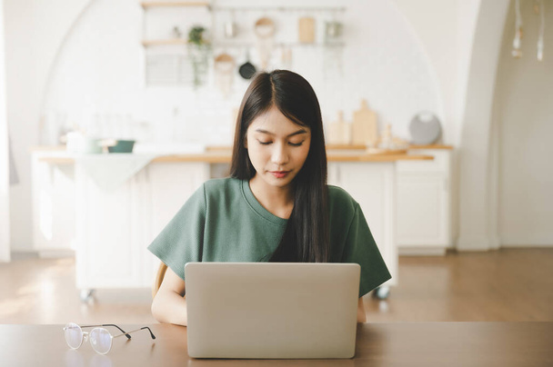 Usmívající se asijská mladá žena pracující na notebooku v domácí kanceláři. Mladý asijský student pomocí počítače dálkové studium, virtuální školení, e-learning, sledování online vzdělávání webinář v domě - Fotografie, Obrázek