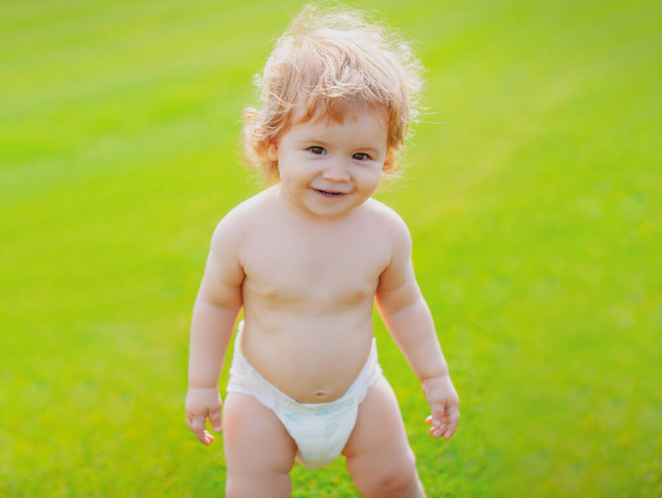 Little baby in diaper playing in nature on the green grass. Kids playing. Baby and summer sunny weather. Funny little child closeup portrait. Blonde kid, laughing emotion, happy smiling face. - Foto, immagini