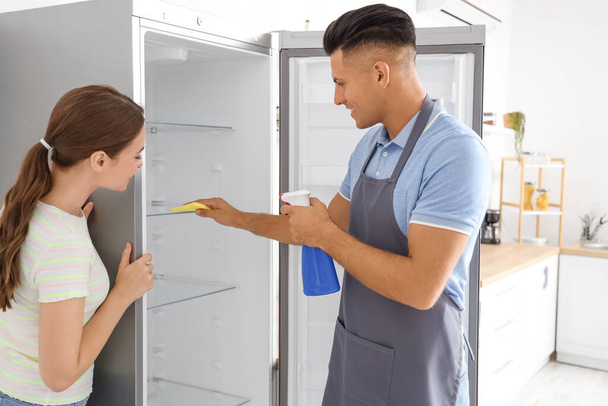 Junges Paar putzt Kühlschrank in Küche - Foto, Bild
