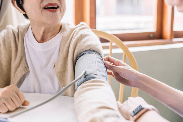 Sluit verpleegkundige hand meten van de bloeddruk van senior vrouw met zorg. Caregiver bezoek thuis. Begrip thuiszorg en verpleeghuis. - Foto, afbeelding