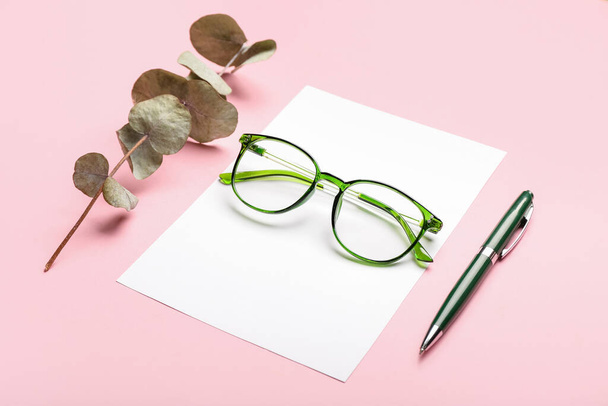 Eyeglasses, sheet of paper, pen and dried eucalyptus branch on color background - Photo, Image