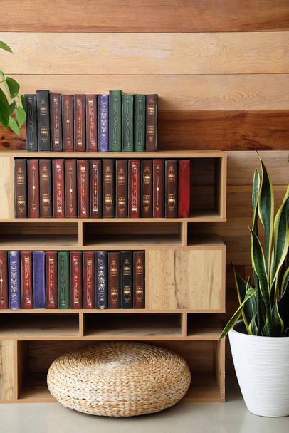 Stylish bookcase with houseplants and pouf near wooden wall - Zdjęcie, obraz
