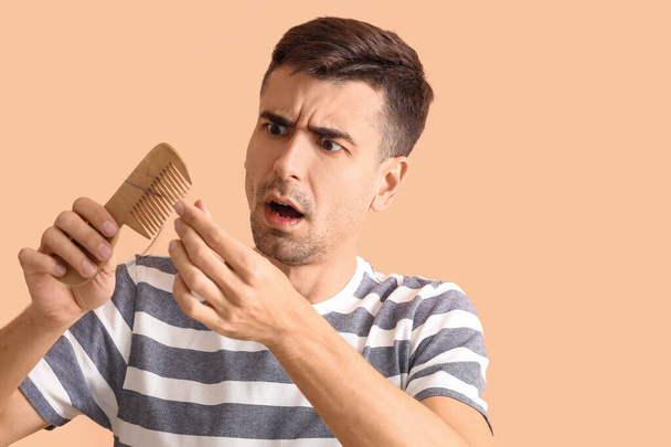 Shocked young man holding comb with fallen down hair on beige background - Photo, Image
