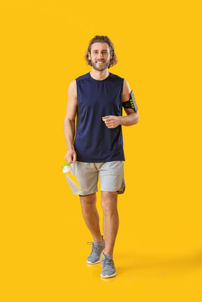 Sportieve man met flesje water op oranje achtergrond - Foto, afbeelding