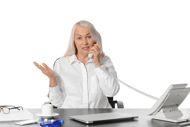 Mature secretary talking by phone at table on white background - Foto, imagen