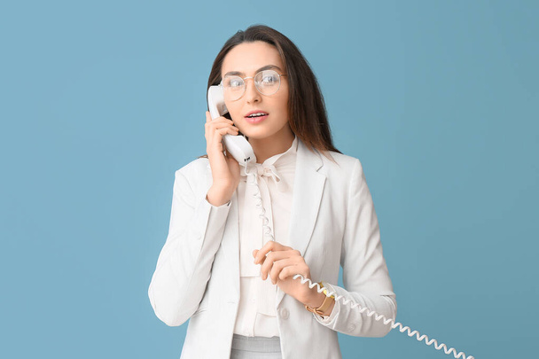Portrait of young secretary talking by phone on blue background - Foto, Imagen