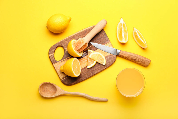 Composition with cut lemons, juicer and glass of juice on yellow background - Фото, изображение