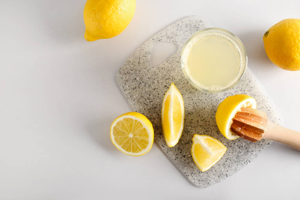 Σύνθεση με λεμόνια, αποχυμωτή και ποτήρι χυμό σε ανοιχτό φόντο - Φωτογραφία, εικόνα
