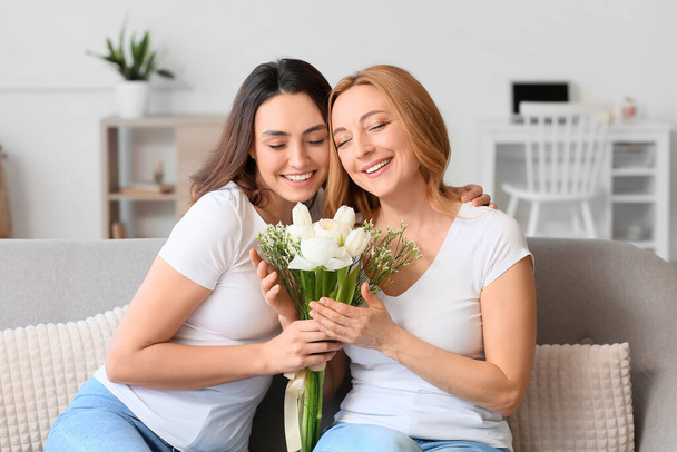 Young woman and her mother with flowers on International Women's Day at home - 写真・画像