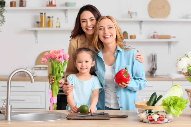 Счастливая молодая женщина, ее маленькая дочь и мать на кухне дома. Международный женский день - Фото, изображение