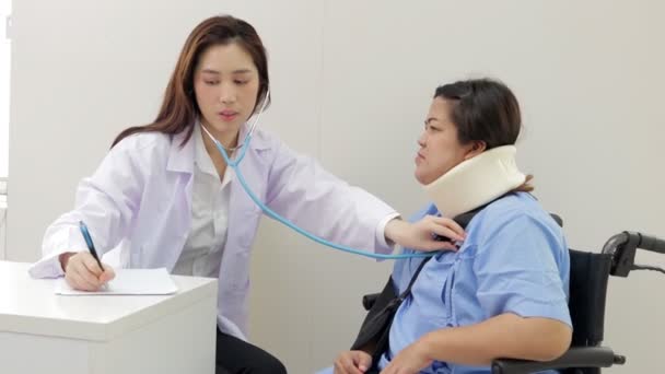 Médica asiática usar um estetoscópio para ouvir o ritmo cardíaco de pacientes obesos Sentado em uma cadeira de rodas na sala de exame. conceito de serviços médicos em um hospital - Filmagem, Vídeo
