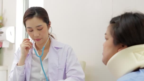 Азиатская женщина-врач использует стетоскоп, чтобы слушать ритм сердца пациентов с ожирением, сидящих в инвалидной коляске в комнате обследования. концепция медицинских услуг в стационаре - Кадры, видео