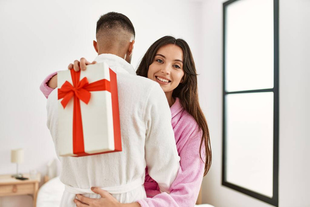 Jeune couple hispanique souriant heureux surprenant avec cadeau à la chambre. - Photo, image