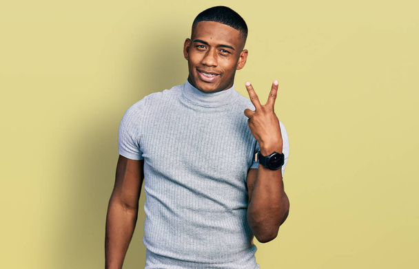Young black man wearing casual t shirt smiling with happy face winking at the camera doing victory sign with fingers. number two.  - Foto, Bild