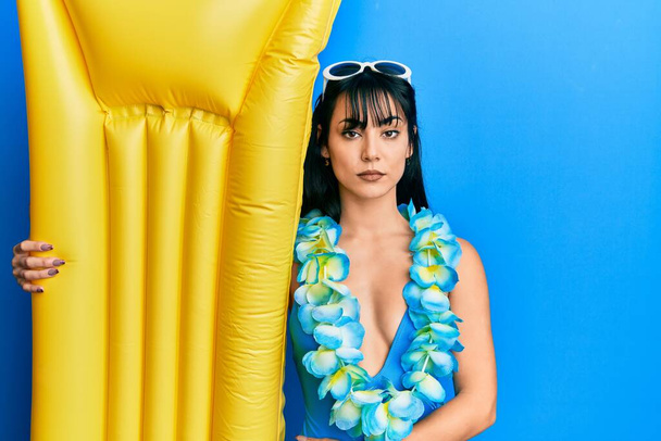 Young brunette woman with bangs wearing swimsuit and holding summer float thinking attitude and sober expression looking self confident  - Photo, image