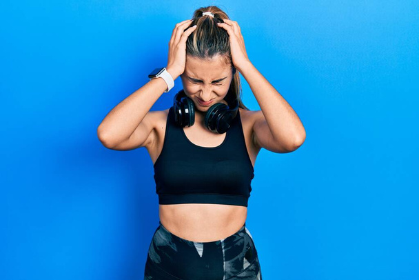 Beautiful hispanic woman wearing gym clothes and using headphones suffering from headache desperate and stressed because pain and migraine. hands on head.  - Photo, Image