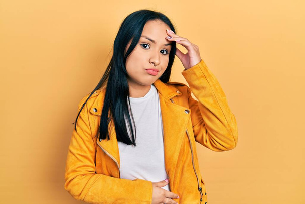 Beautiful hispanic woman with nose piercing wearing yellow leather jacket worried and stressed about a problem with hand on forehead, nervous and anxious for crisis  - Foto, imagen
