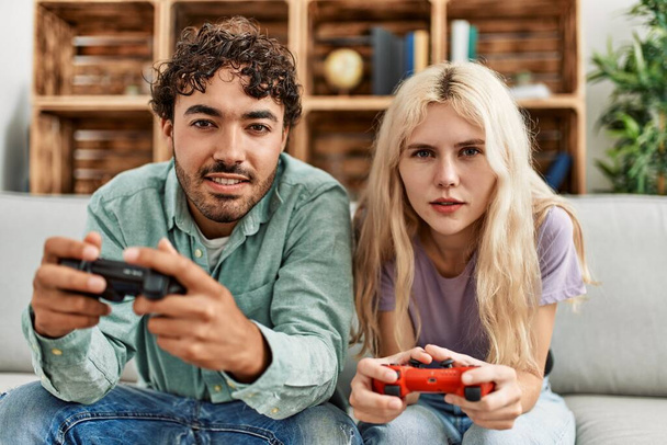 Νεαρό ζευγάρι χαμογελά ευτυχισμένος παίζοντας βιντεοπαιχνίδι στο σπίτι. - Φωτογραφία, εικόνα