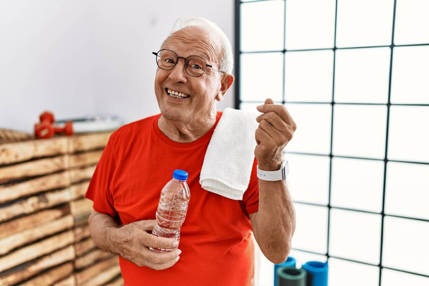 Старший мужчина в спортивной одежде и полотенце в тренажерном зале делает итальянский жест с уверенным выражением рук и пальцев  - Фото, изображение
