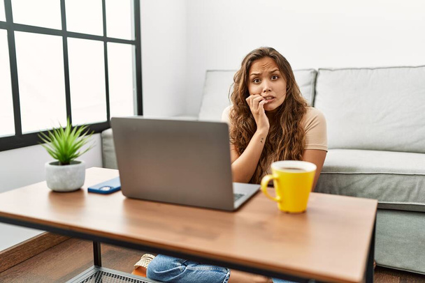 Beautiful hispanic woman using computer laptop at home looking stressed and nervous with hands on mouth biting nails. anxiety problem.  - Photo, Image