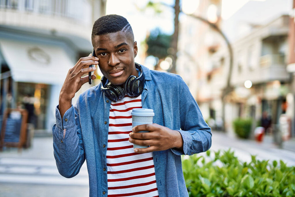 Νεαρός Αφροαμερικάνος που μιλάει στο smartphone πίνοντας καφέ στην πόλη. - Φωτογραφία, εικόνα