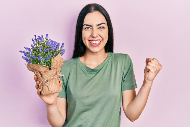 Mooie vrouw met blauwe ogen houden lavendel plant schreeuwen trots, vieren overwinning en succes zeer enthousiast met opgeheven arm  - Foto, afbeelding