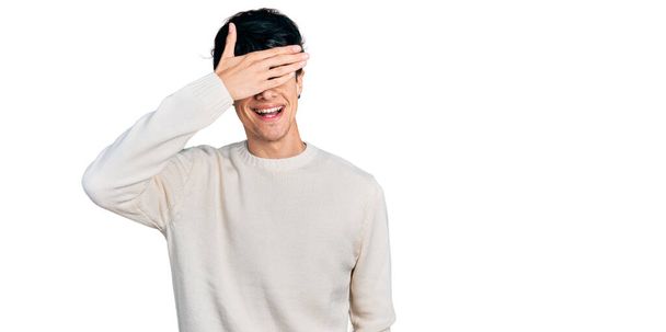 Bello hipster giovane uomo che indossa casual maglione invernale sorridente e ridente con mano sul viso che copre gli occhi per la sorpresa. concetto cieco.  - Foto, immagini