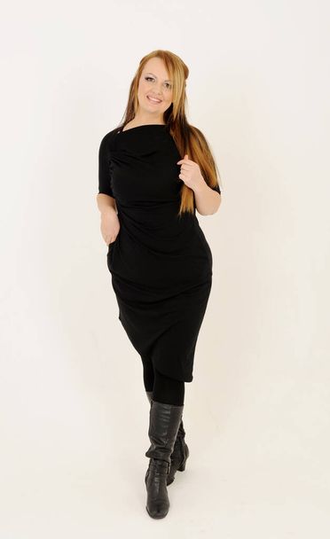 Eine erwachsene Frau von europäischem Aussehen mit langen Haaren und hellem Make-up in dunkler Kleidung für Werbung auf hellem Hintergrund - Foto, Bild