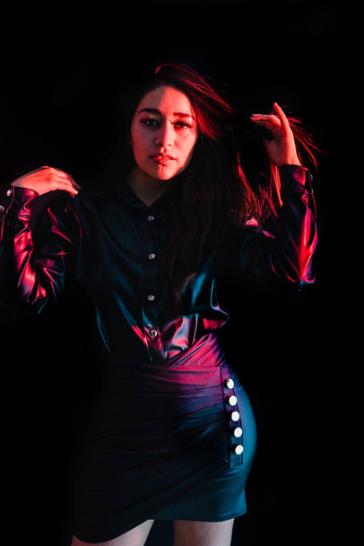 young latin woman dressed in black clothes with colorful pink-blue lights on black background in Mexico Latin America - Φωτογραφία, εικόνα