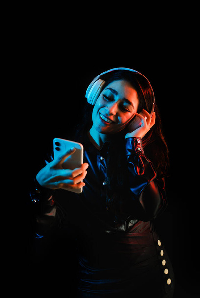 latin young woman with headphones listening to music over color neon and black background in Mexico Latin America - Foto, Imagen