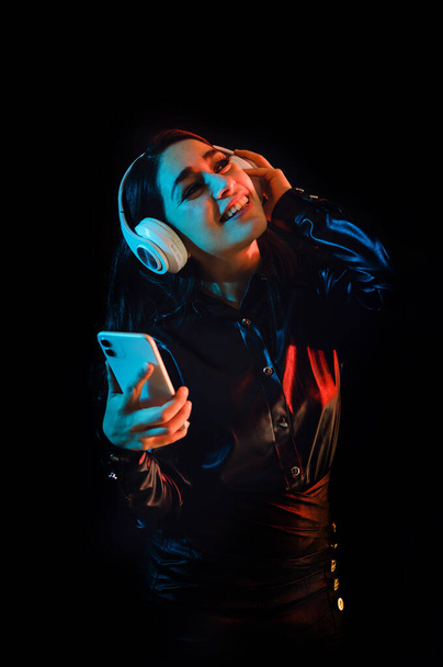 jeune femme latine avec écouteurs écoutant de la musique sur fond néon couleur et noir au Mexique Amérique latine - Photo, image