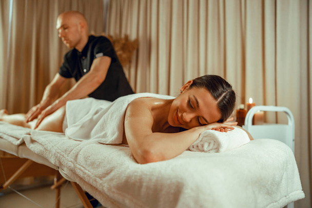 Женщина лежит с закрытыми глазами, наслаждаясь профессиональным массажем в спа-центре - Фото, изображение